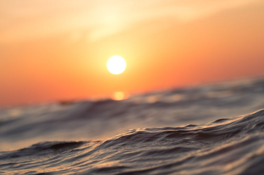 Close-up of rippling ocean water at sunset with the sun glowing on the horizon